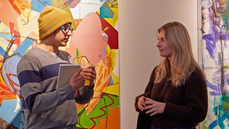 U N E students talk in front of two large colorful paintings in U N E's Portland Art Gallery